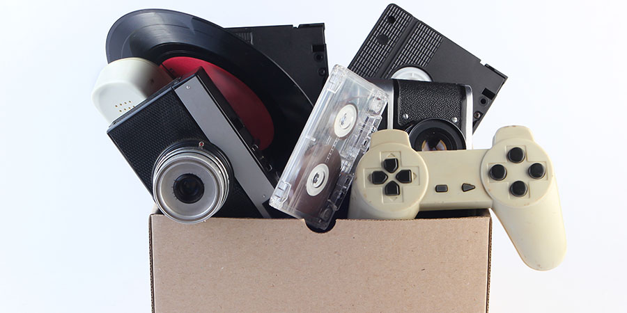 Cardboard box with video cassettes, retro film camera, vinyl record, audio cassette, gamepad on a white background